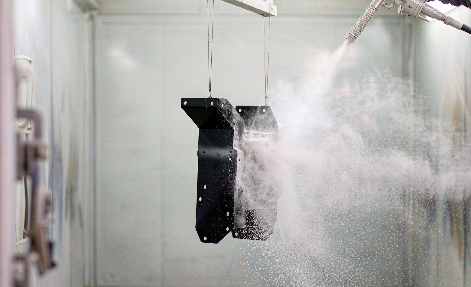 Steel bracket on a conveyor being powder coated inside a spray booth